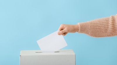 Weibliche Hand wirft einen Umschlag in eine Wahlurne